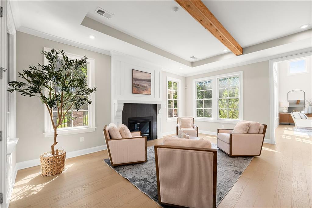 Staged living room with a fireplace, large windows, neutral seating, and an exposed wood ceiling beam.