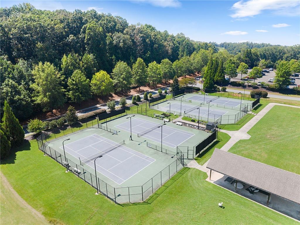 Aerial view of multiple fenced tennis courts beside a pavilion and wooded grounds.