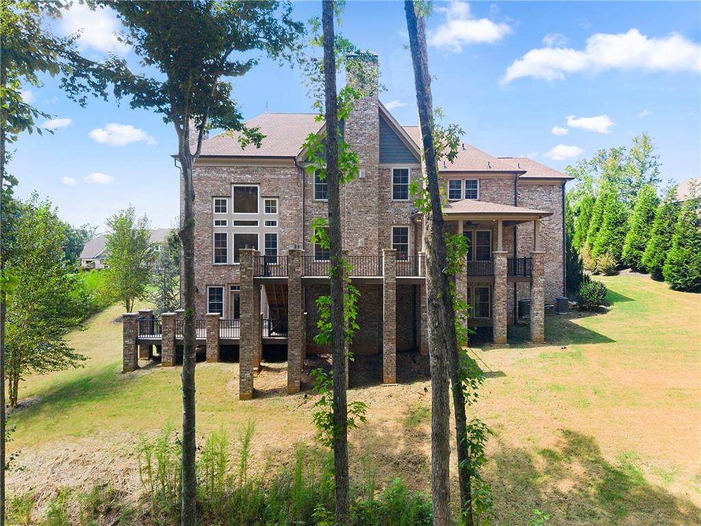 Rear of a multilevel brick house with elevated decks and a covered patio among mature trees.