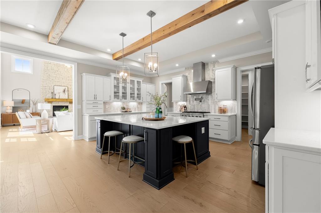 Open-plan kitchen with a large black island, white cabinets, exposed wood beams, and adjoining living area.