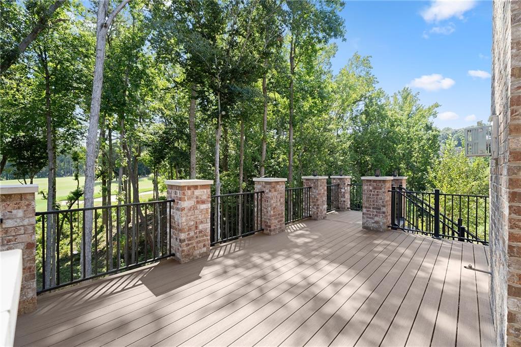 Raised deck with brick columns and black railings overlooking mature trees and a grassy open area.