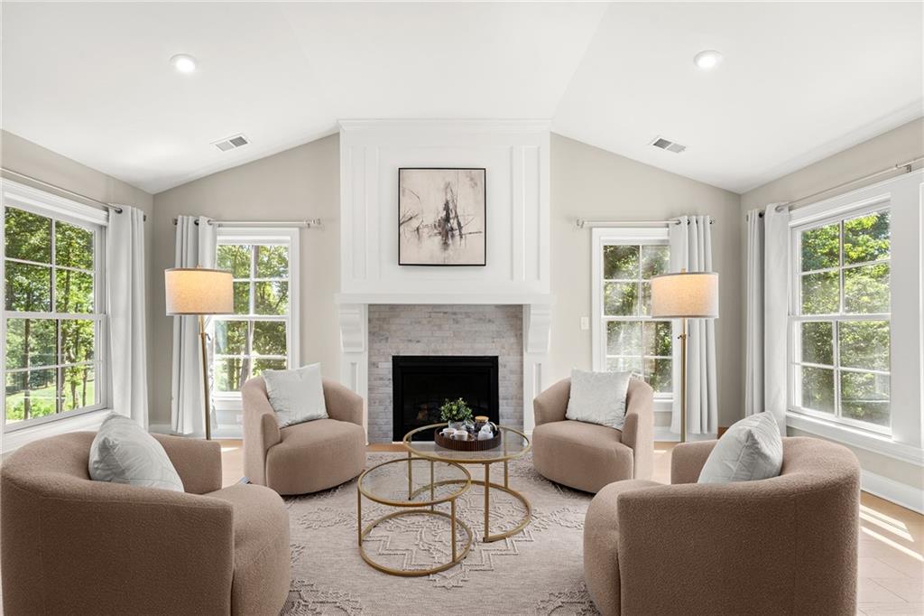Bright living room with a fireplace, four chairs, and large curtained windows.