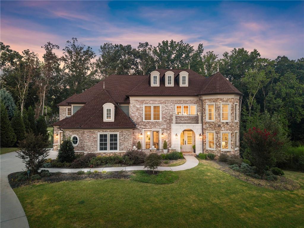 Brick and stone home with multiple dormers, a rounded bay, and landscaped front lawn at dusk.