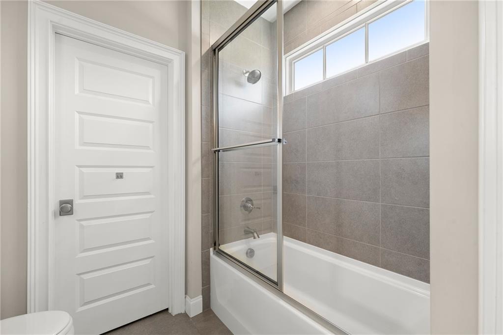 Bathroom with a white tub, glass shower screen, gray tile, and high horizontal window.