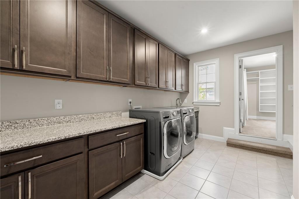 Laundry room with dark wood cabinetry, stone counters, front-loading washer and dryer, and adjoining walk-in closet.