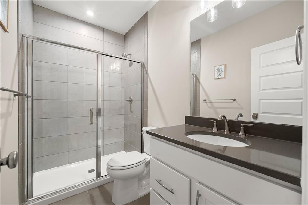 Bathroom with a tiled glass-enclosed shower, toilet, and dark-countertop vanity.