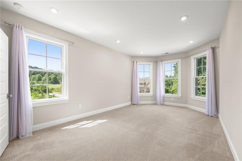 Empty carpeted bedroom with large curtained windows overlooking greenery.