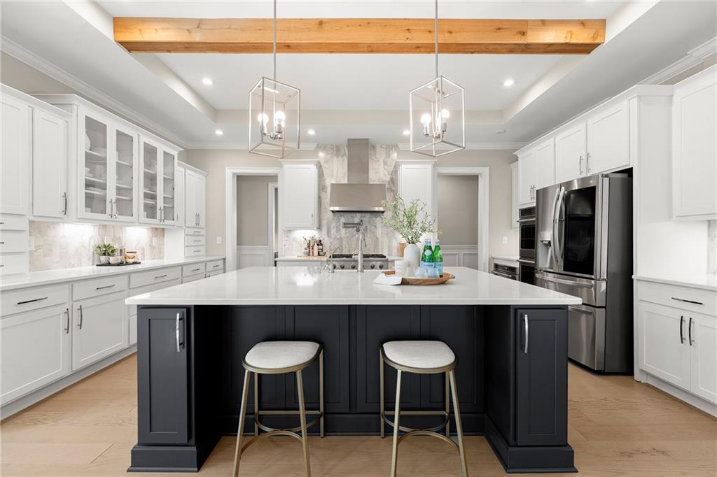 Bright kitchen with a large dark island, white cabinetry, stainless steel appliances, and a wood ceiling beam.