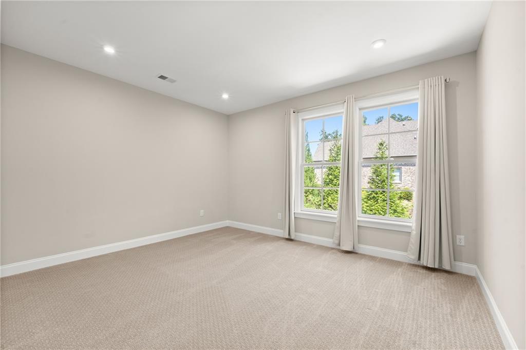 Empty carpeted bedroom with two curtained windows overlooking greenery.