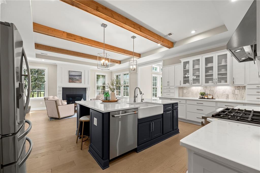 Open kitchen with a navy island, farmhouse sink, and exposed wood ceiling beams.