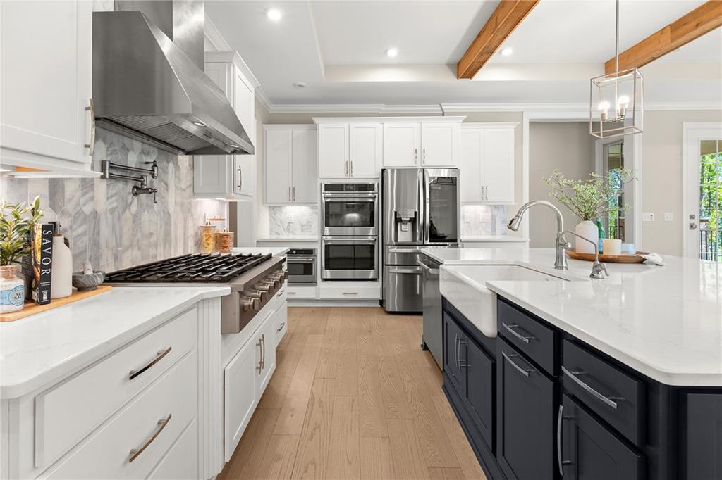 Kitchen with a dark blue island, white cabinets, stainless steel appliances, and exposed wood ceiling beams.