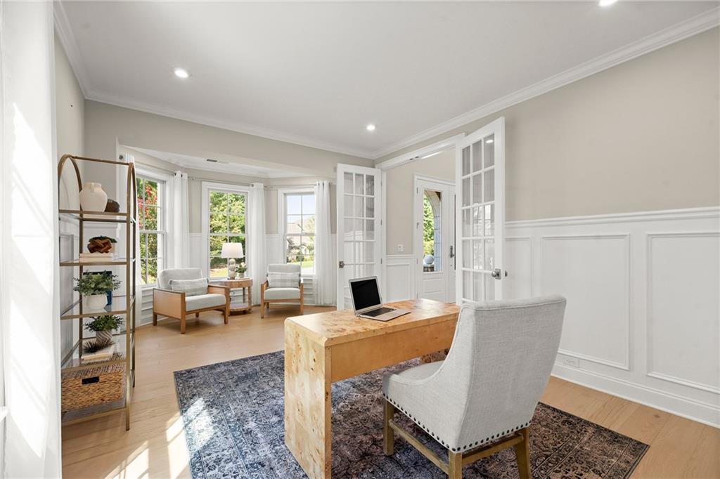 Bright home office with a wood desk, French doors, paneled walls, and windows overlooking greenery.