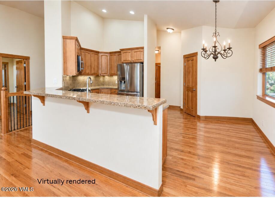 Kitchen and dining area with a granite peninsula, wood cabinetry, stainless steel appliances, and hardwood floors.