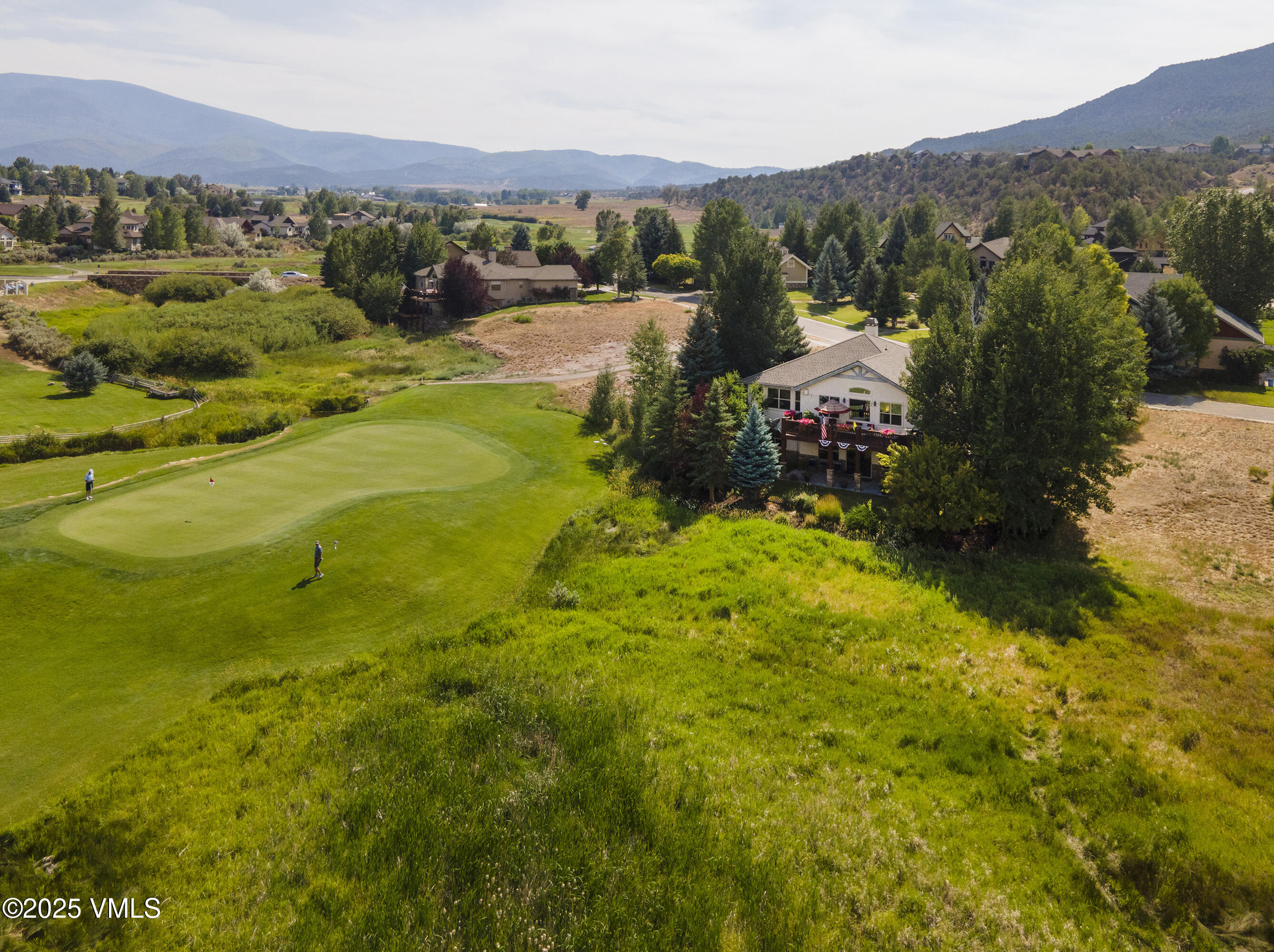 Home beside a golf course, with a raised deck, golfers, and mountains in the distance.