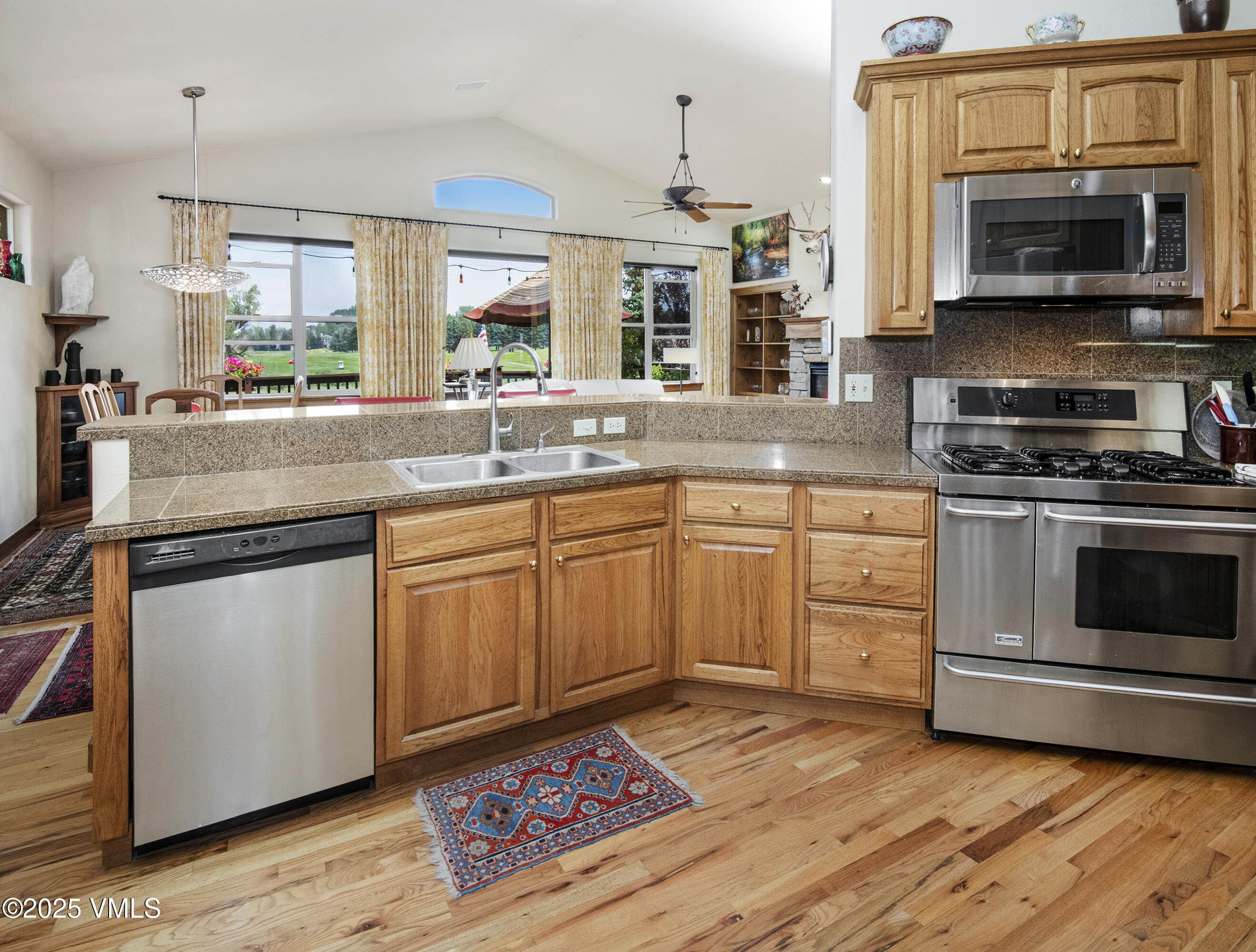 Kitchen with wood cabinets, granite counters, stainless steel appliances, and large windows overlooking a lawn.