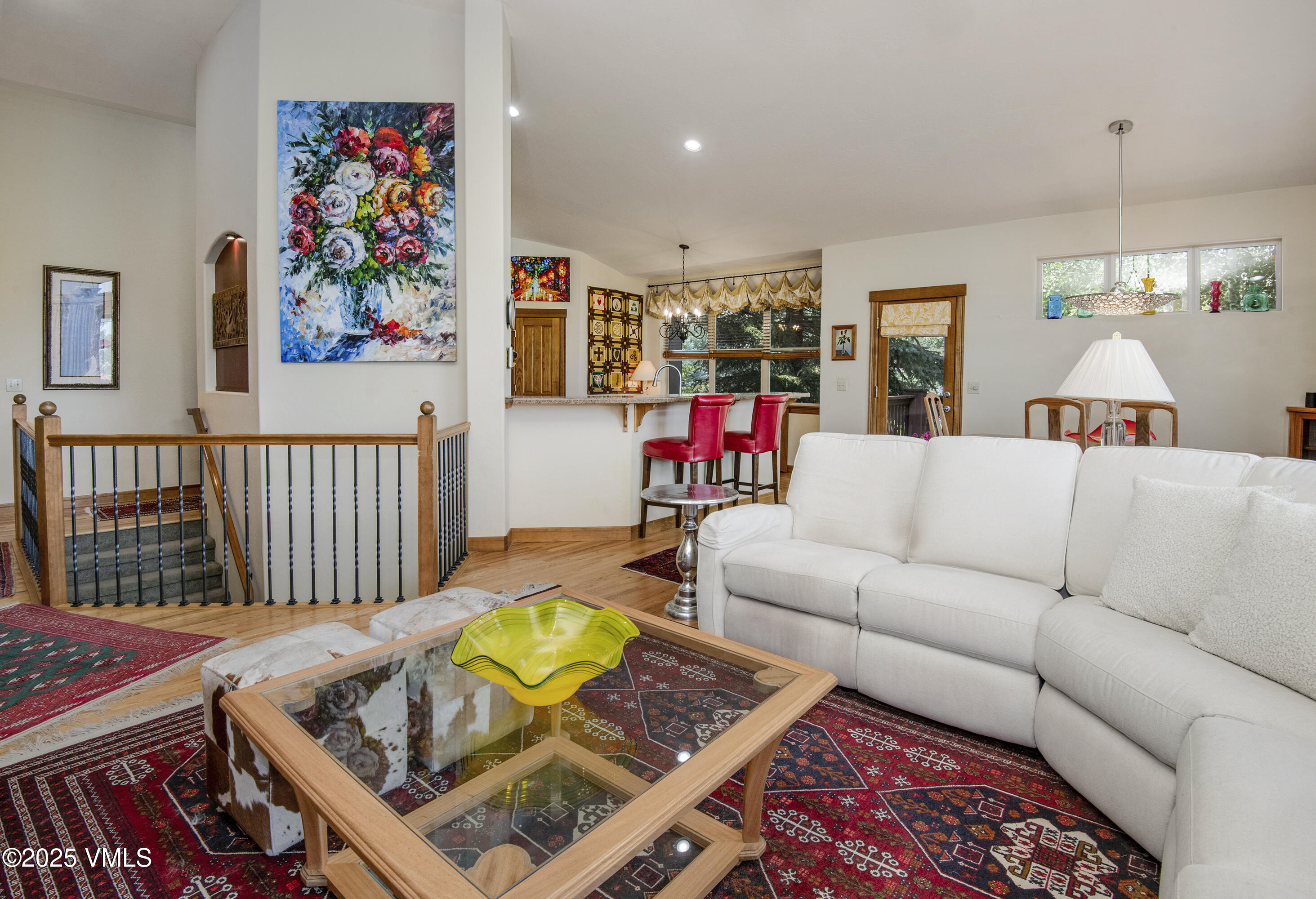 Living room with a white sectional, glass-top coffee table, colorful rugs, and an open kitchen beyond.