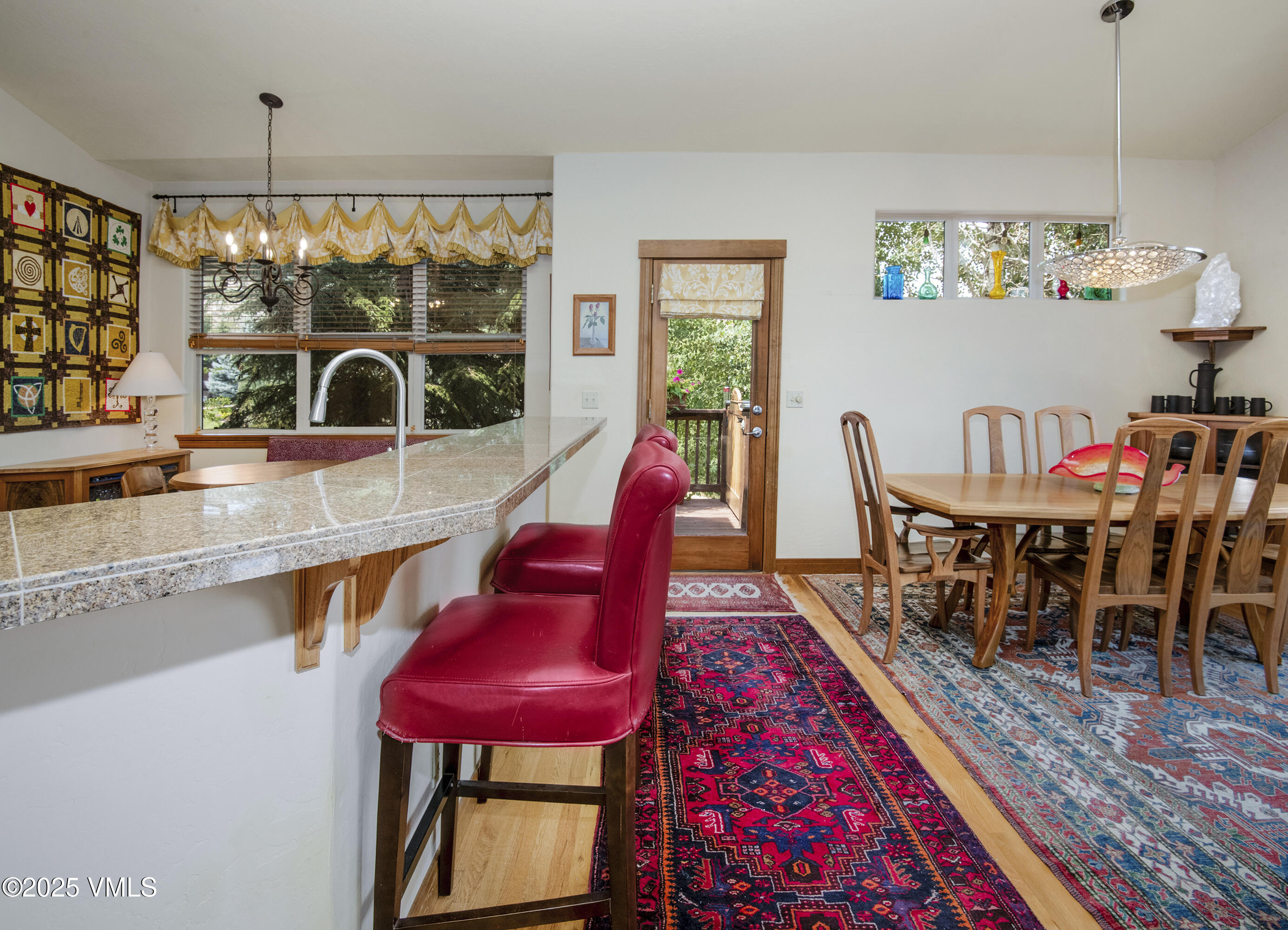 Kitchen and dining area with a granite breakfast bar, red stools, and patterned rugs.