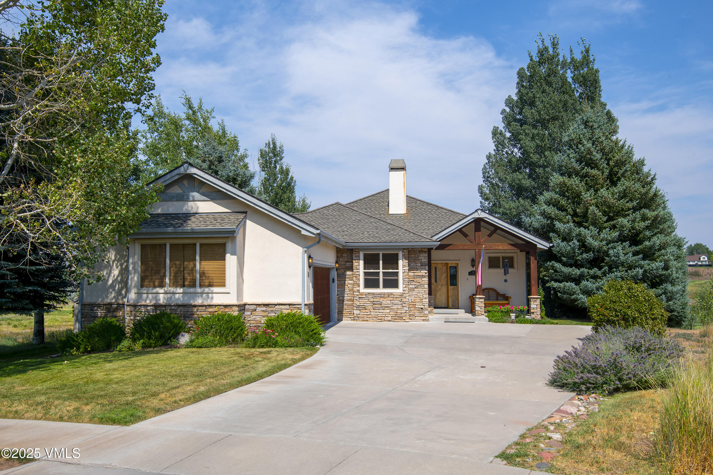 Single-story stone-and-stucco home with a covered porch, broad driveway, and mature trees.