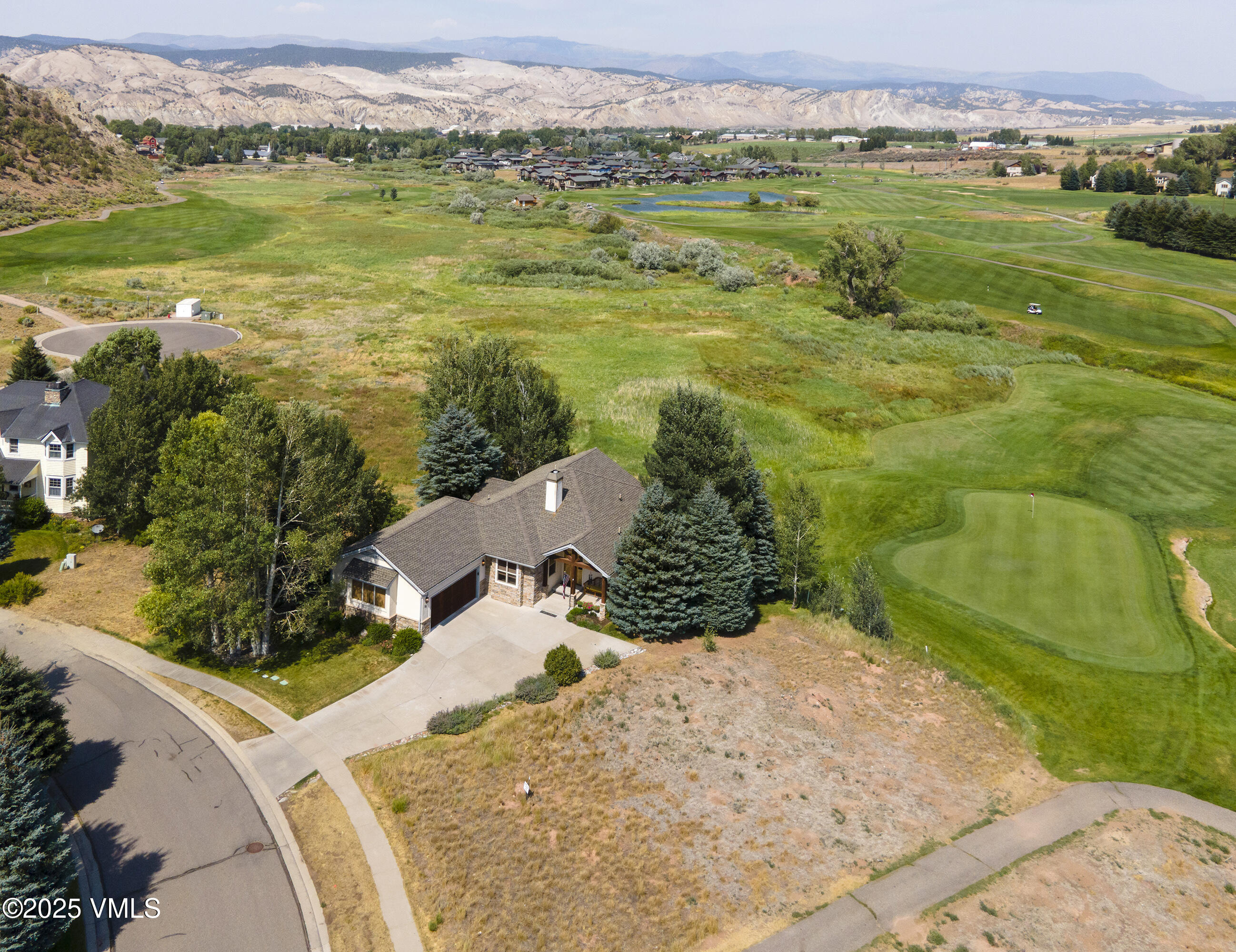 Aerial view of a home beside a golf course, with mountain ranges in the distance.