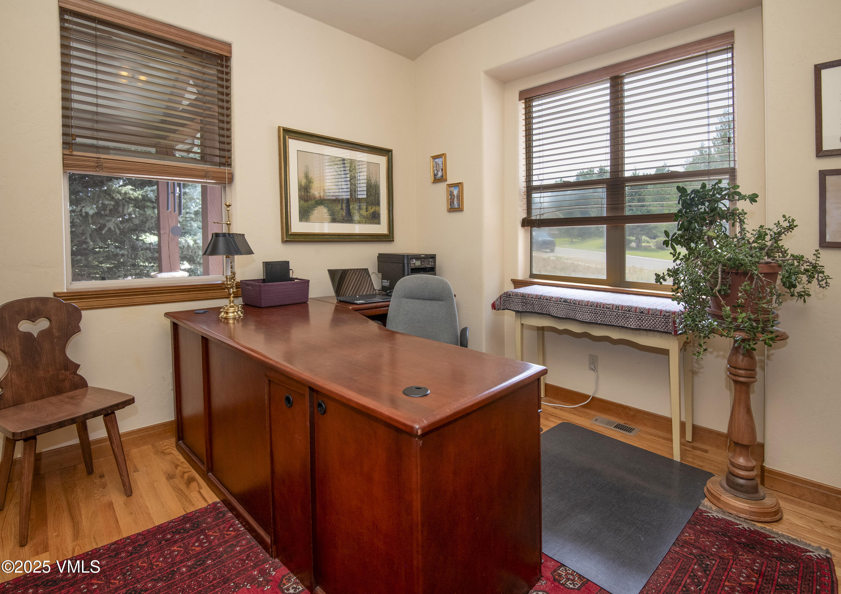 Furnished home office with a large wood desk, hardwood floors, and windows with wooden blinds.