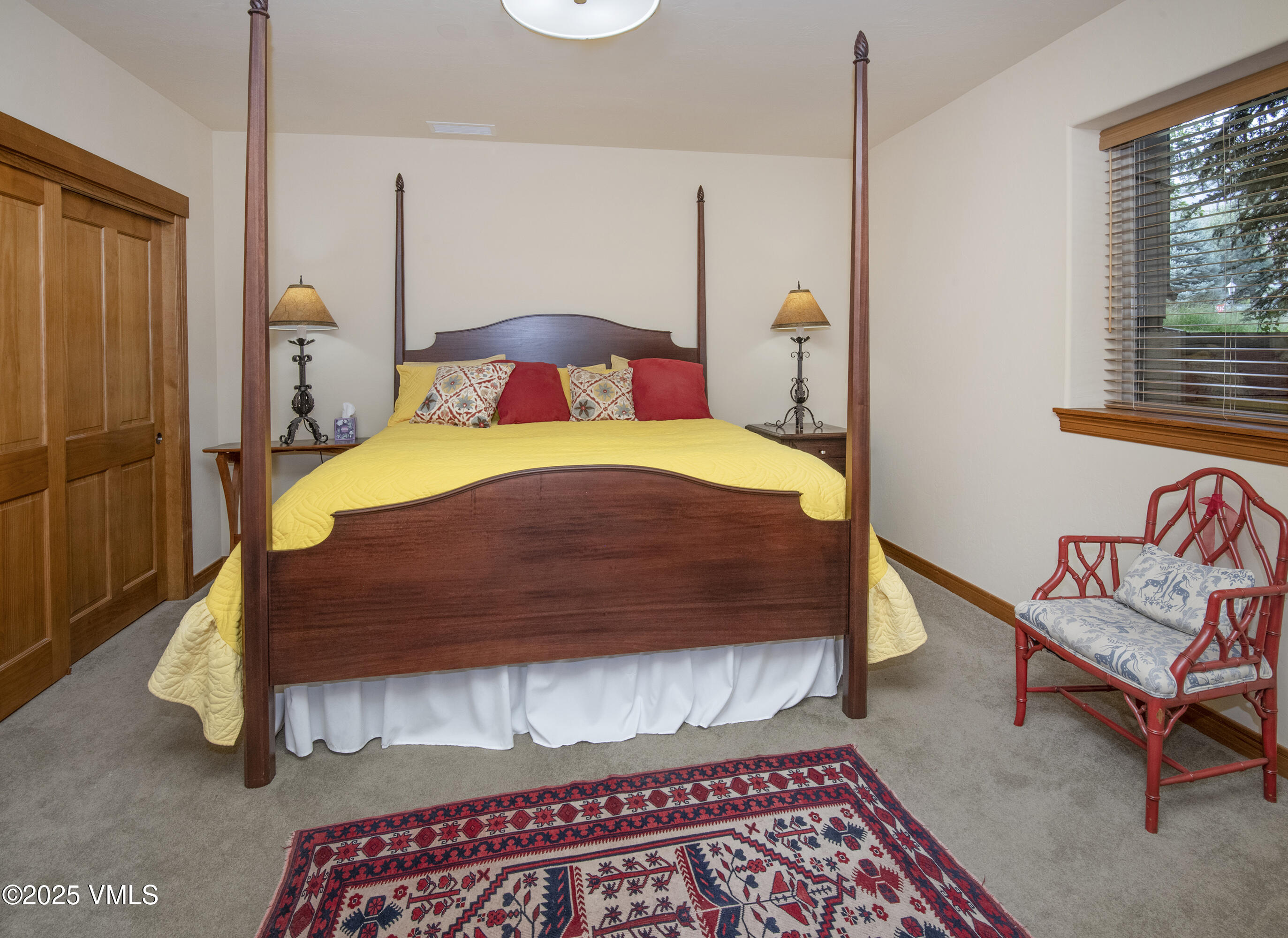 Bedroom with a yellow-quilted four-poster bed, patterned rug, and red chair.