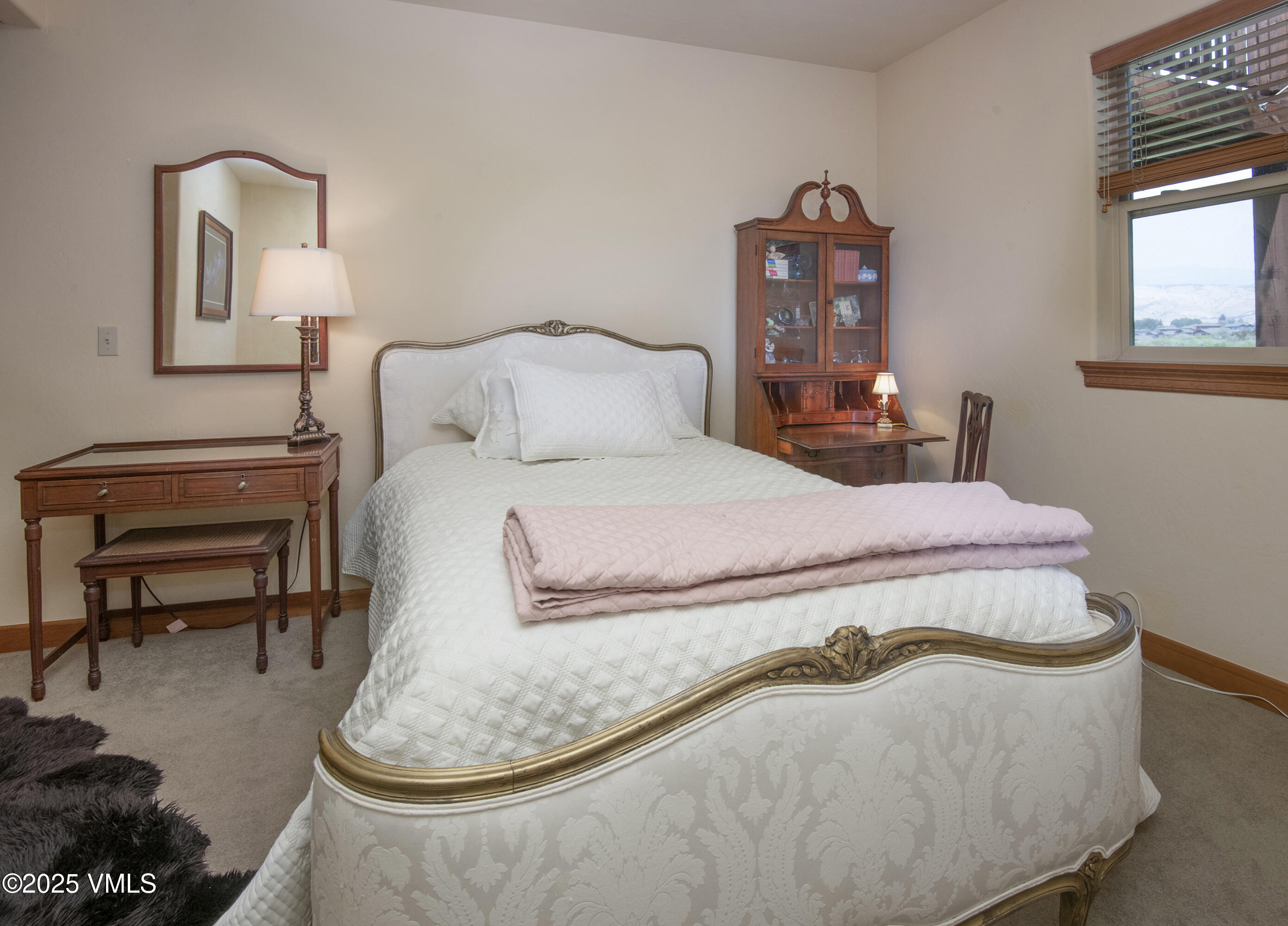 Bedroom with an ornate white bed, carved wooden furniture, and a window overlooking the neighborhood.