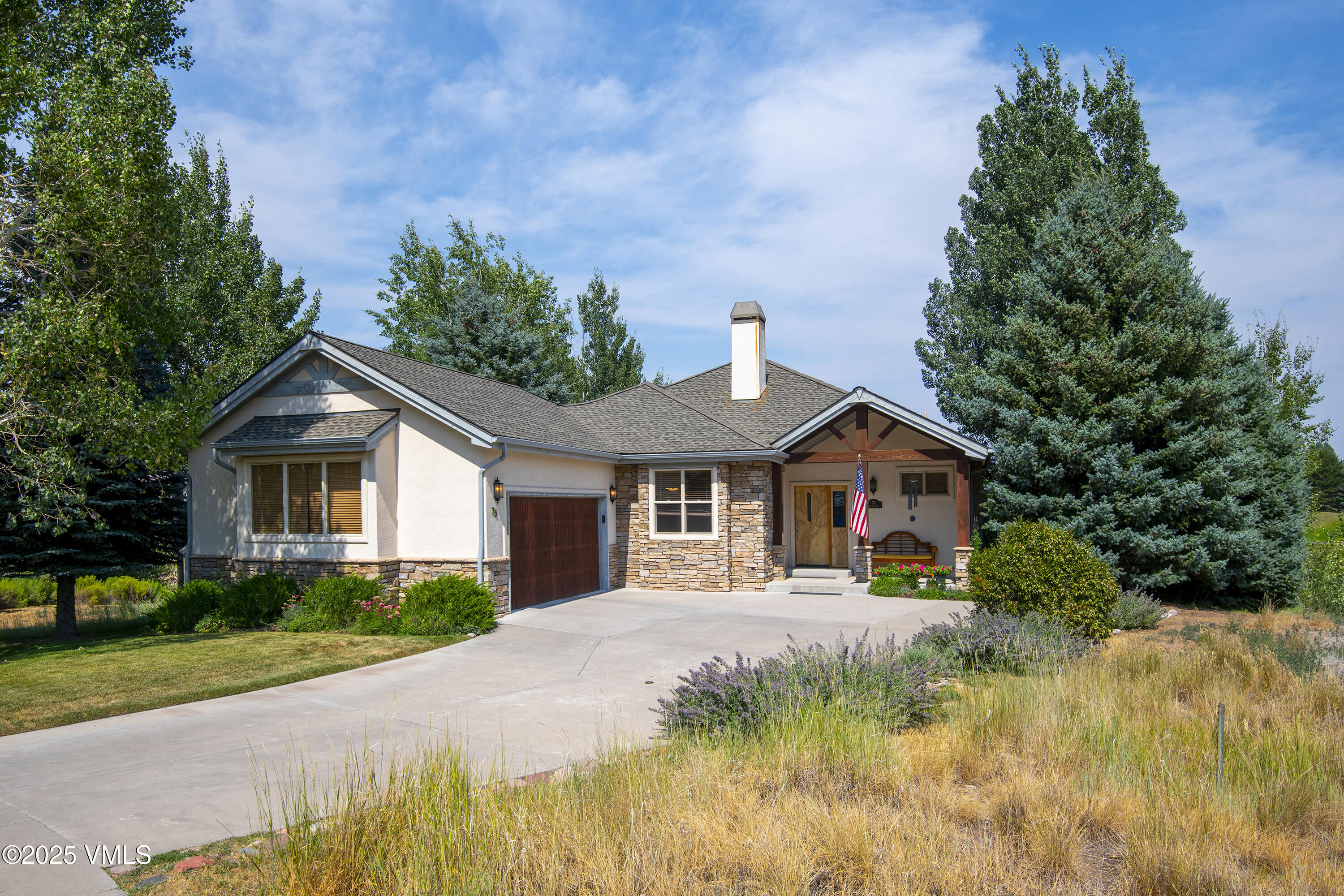Single-story home with stone accents, an attached garage, and a covered porch among mature trees.