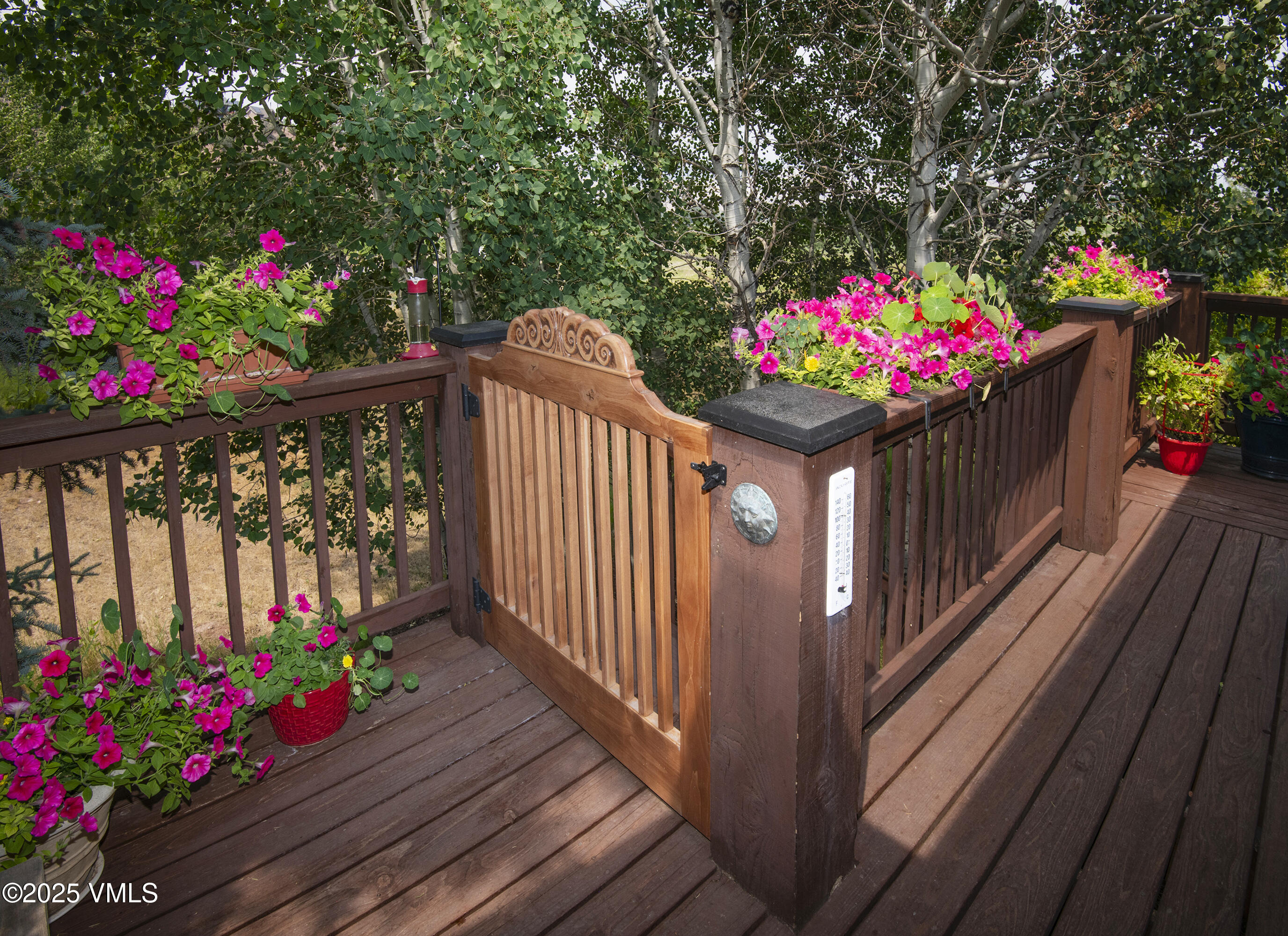 Wooden deck with an ornate gate and bright pink flowers along the railings.