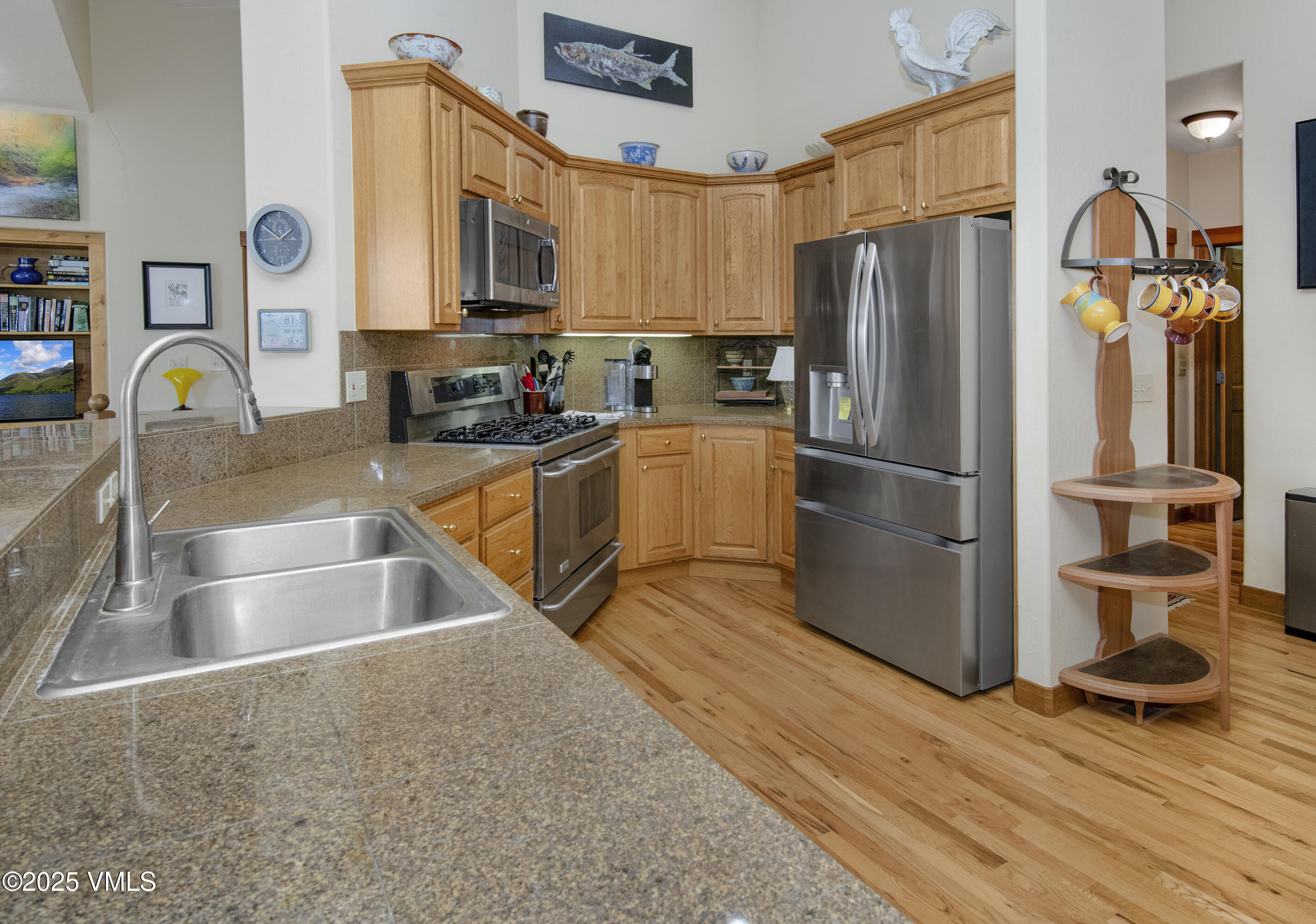 Kitchen with honey-colored wood cabinets, granite counters, stainless steel appliances, and hardwood floors.