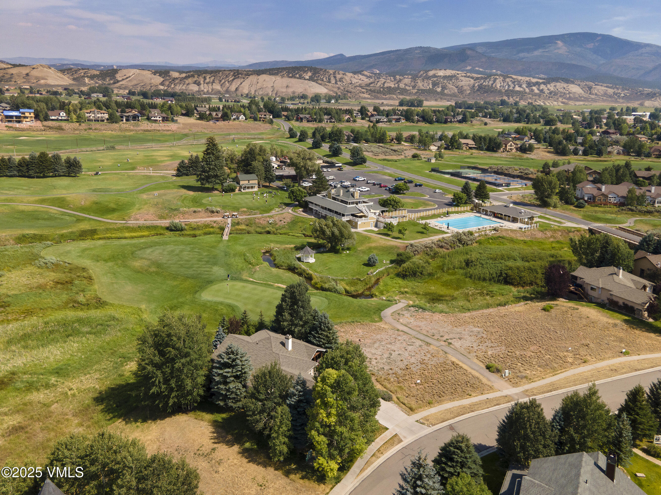 Aerial view of a golf course community with clubhouse, pool, homes, and mountains.