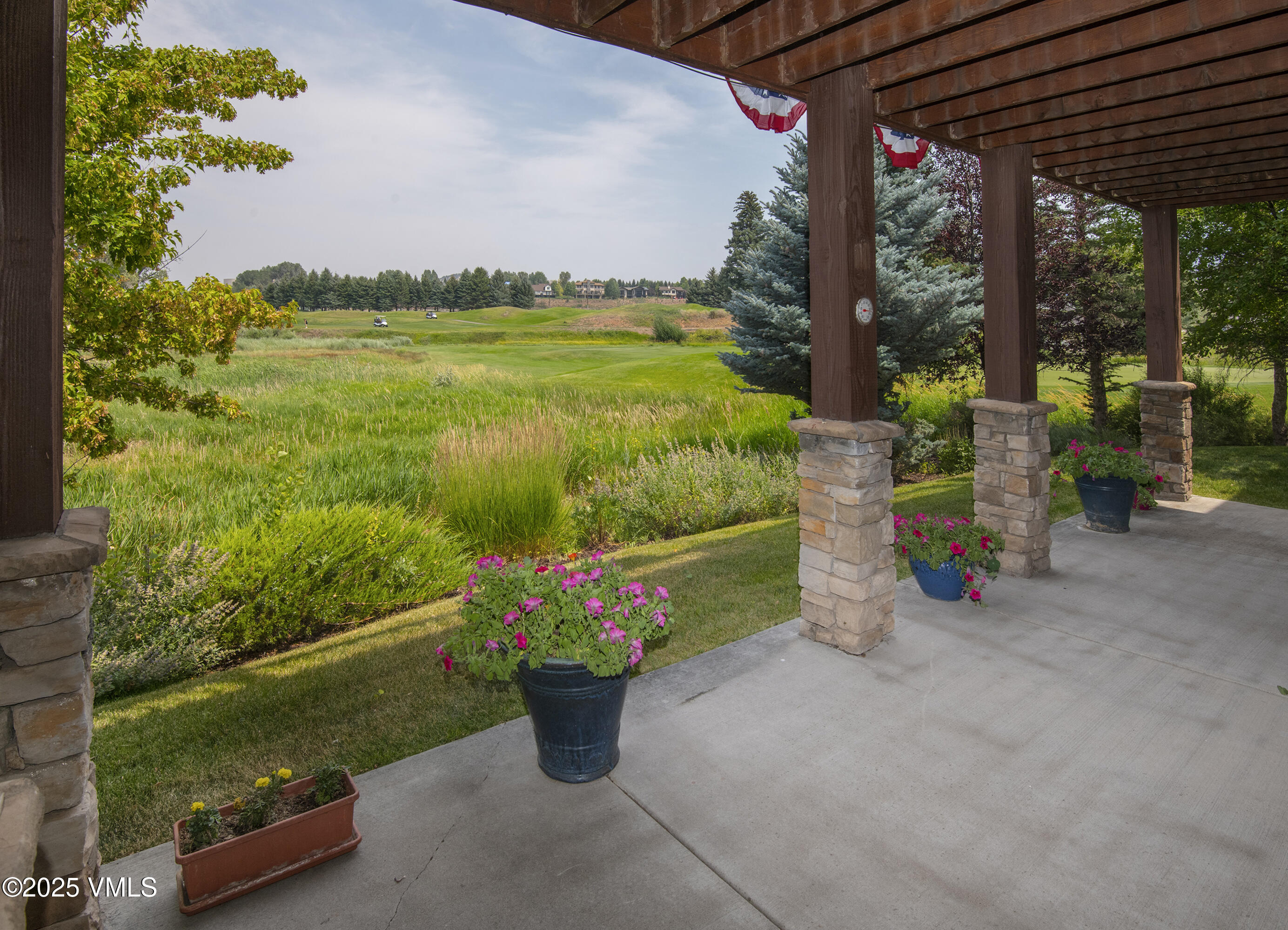 Covered patio overlooking a golf course, with stone columns and pots of pink flowers.