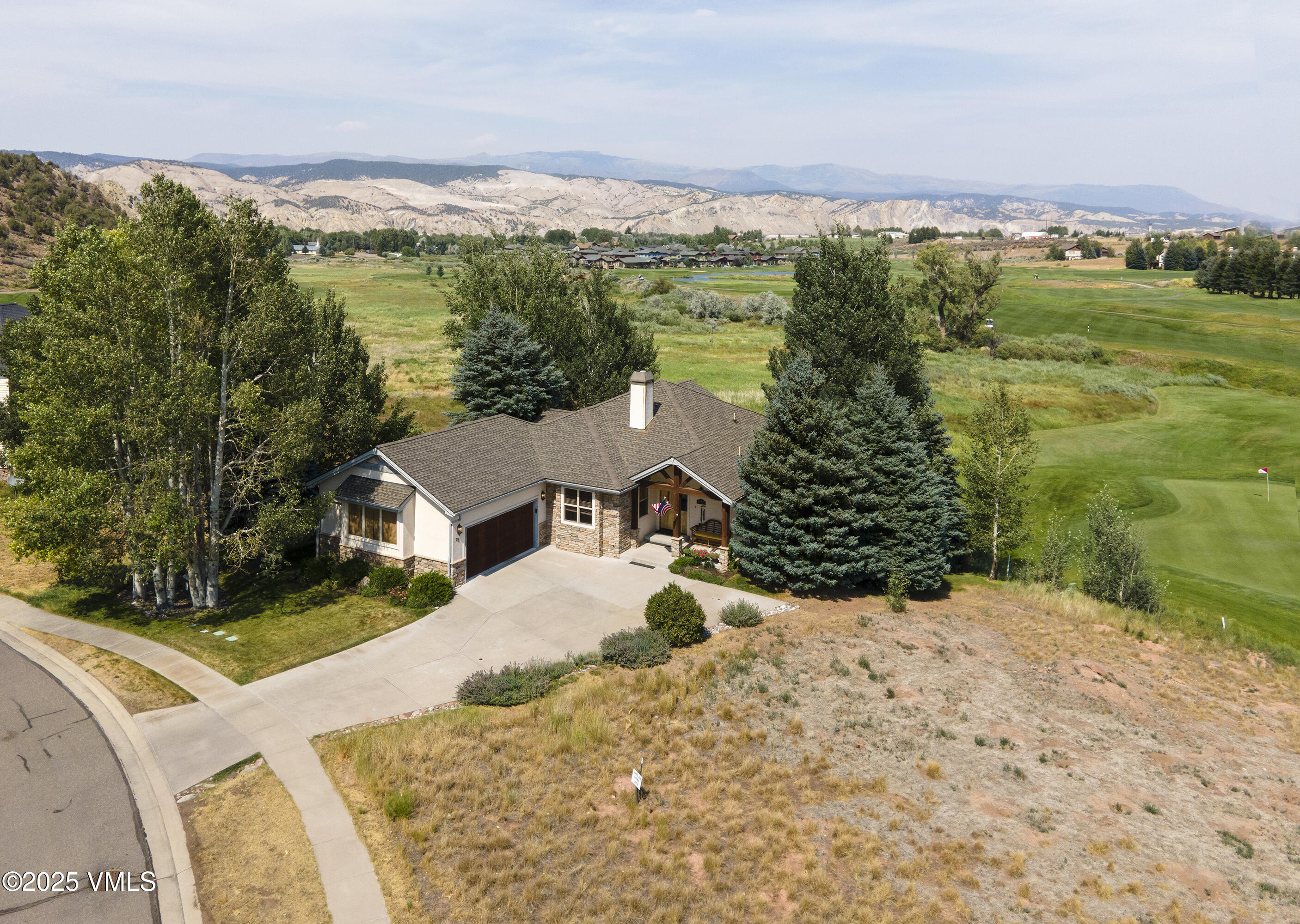 Aerial view of a stone-accented home beside a golf course, with mountains beyond.