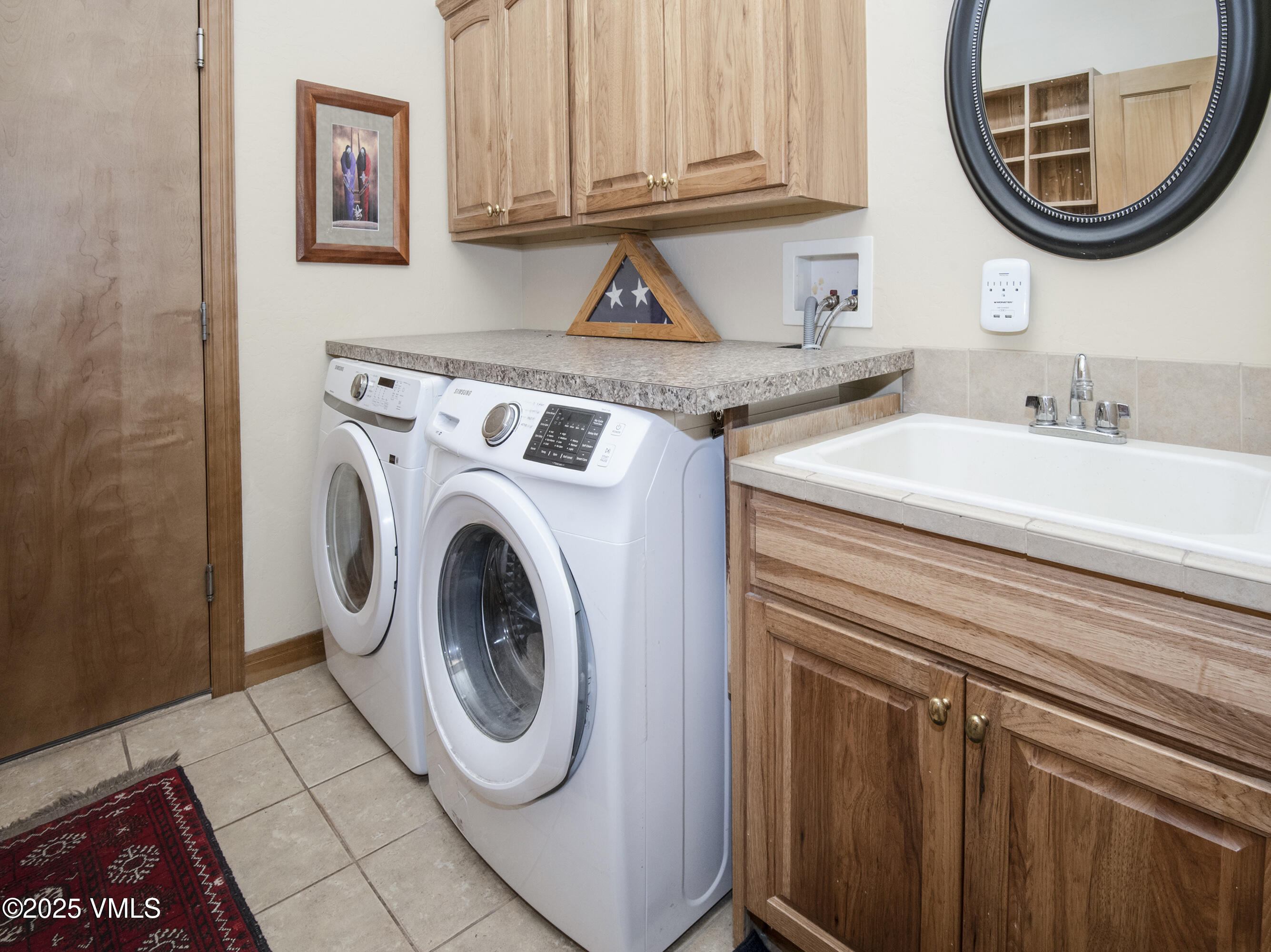 Laundry room with front-loading washer and dryer, wood cabinets, and a utility sink.