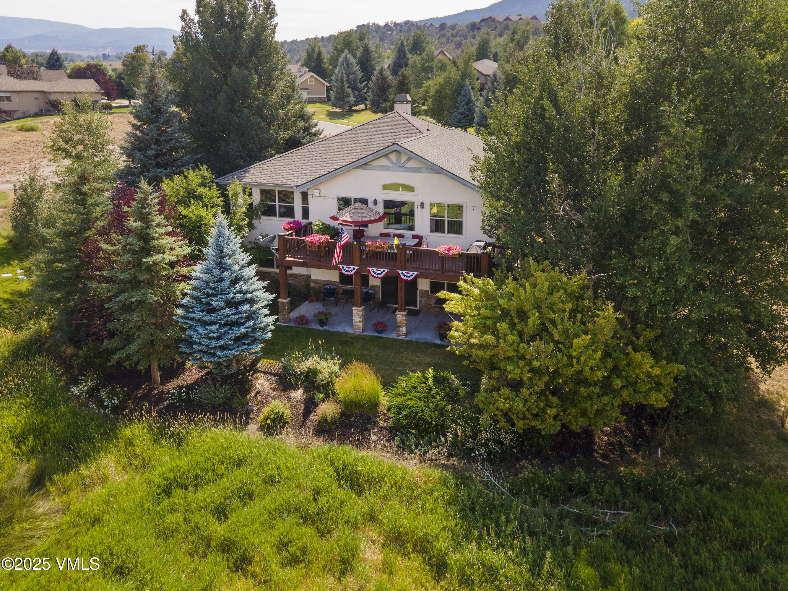 Aerial view of a home with a flower-lined raised deck, landscaped yard, and mountain foothills beyond.