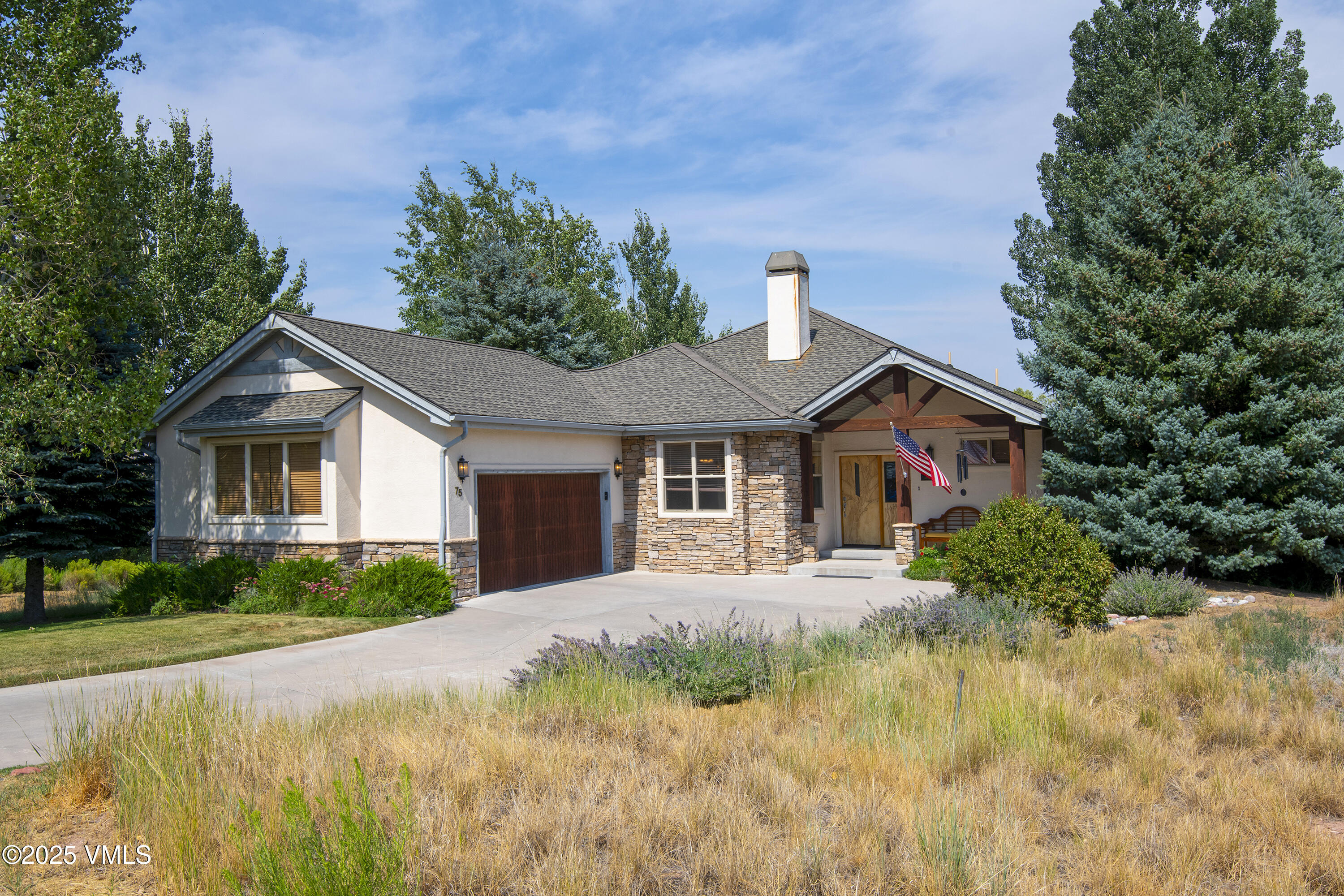 Single-story stone-and-stucco home with an attached garage, covered entry, and American flag.