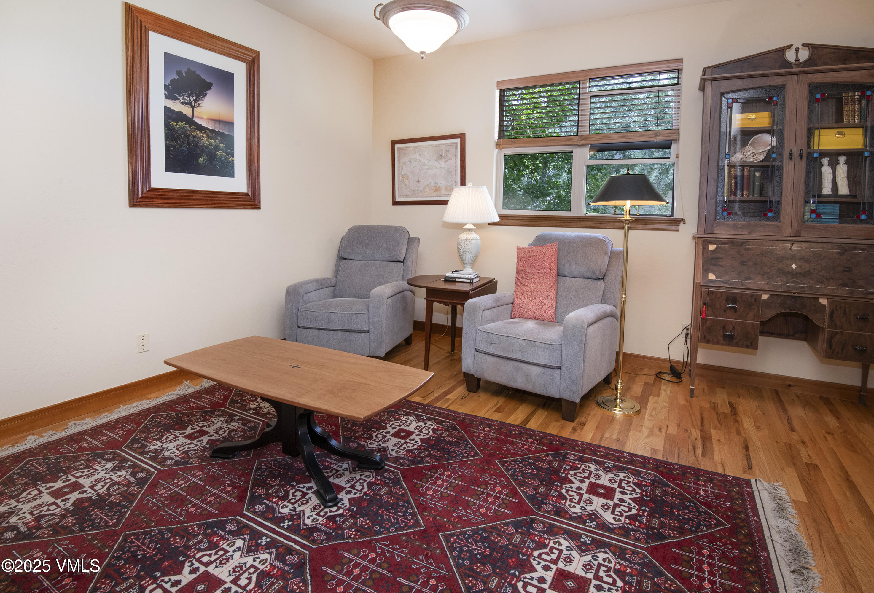 Furnished sitting room with gray armchairs, a red patterned rug, and a dark wooden secretary desk.