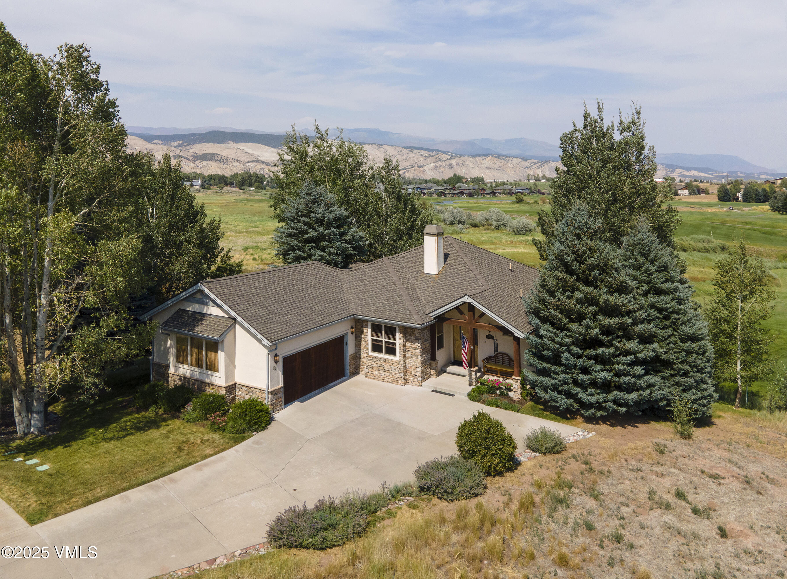 Home with stone accents and a broad driveway, framed by mature trees with golf course and mountains beyond.