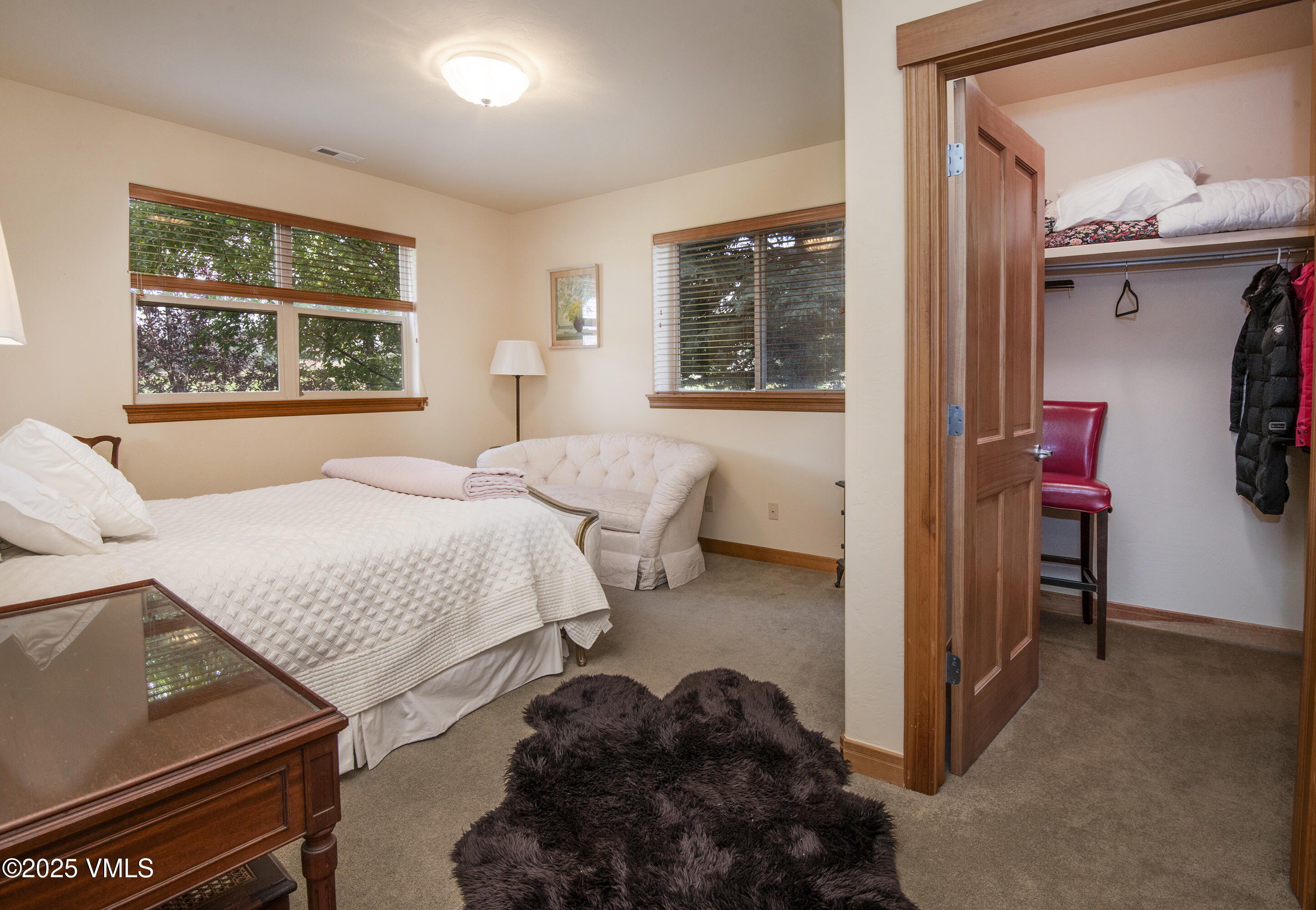 Furnished bedroom with a white quilted bed, large windows, and an open walk-in closet.