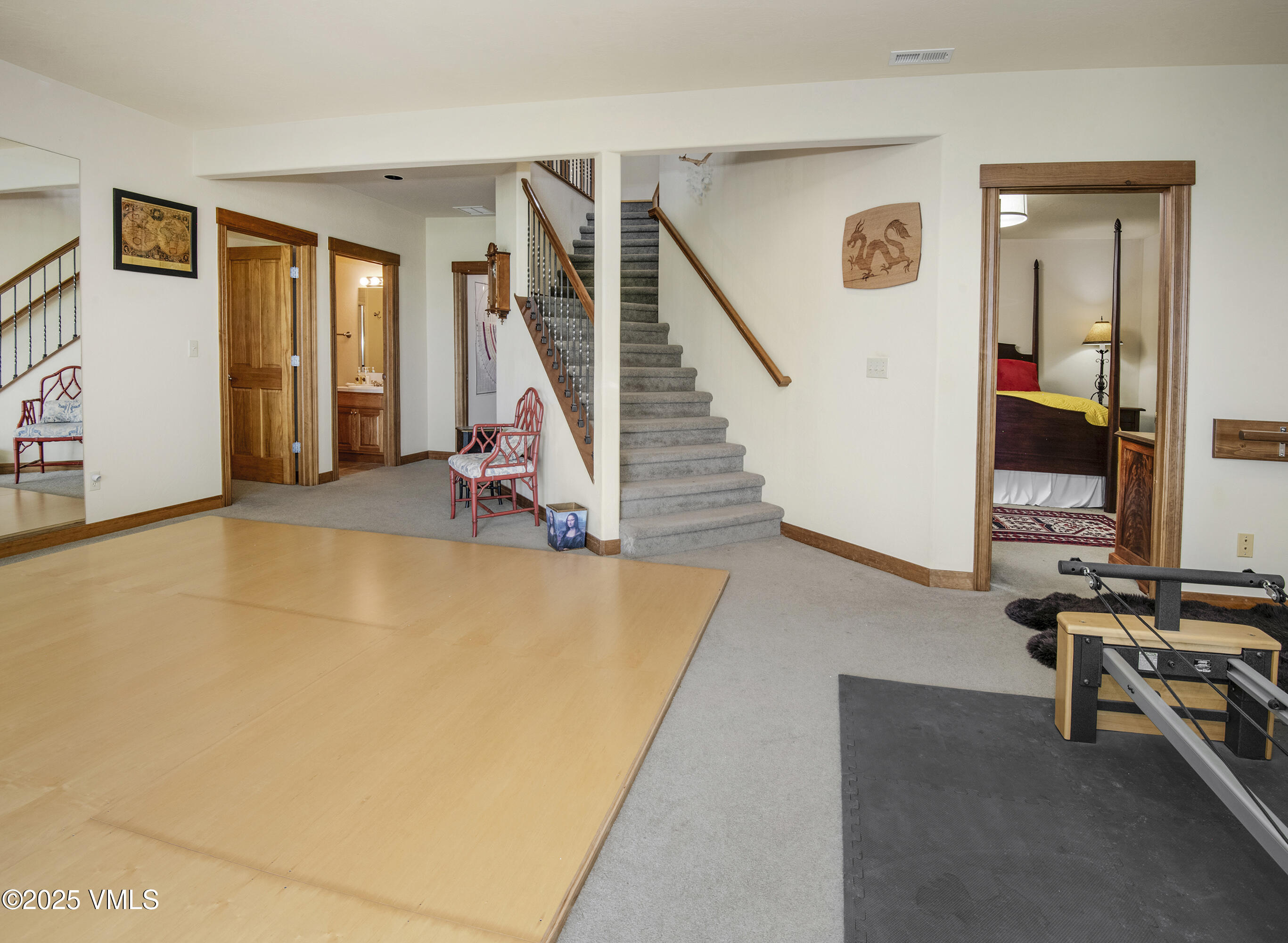 Interior room with a spacious wood-floored area, carpeted stairs, and exercise equipment.