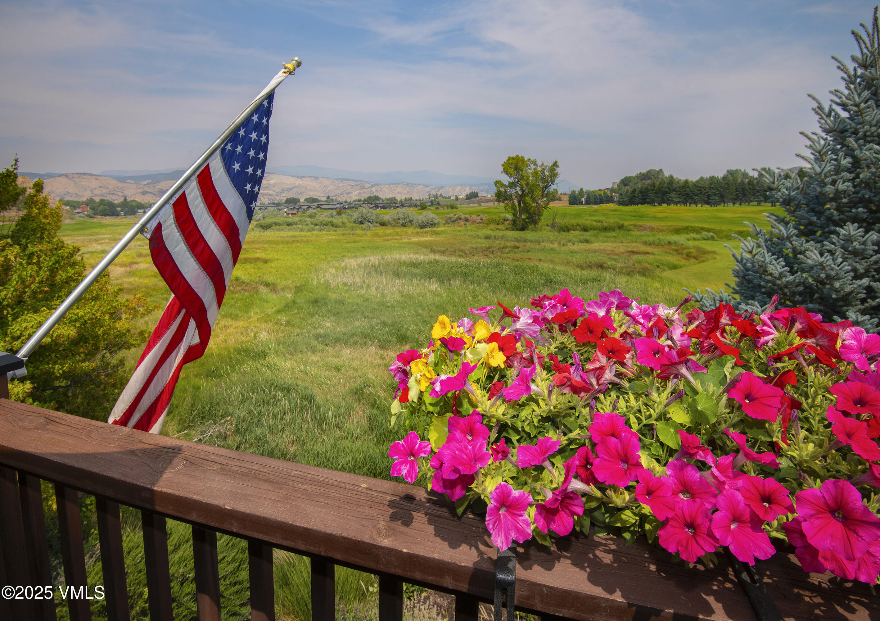 Mountain meadow view from a deck with an American flag and bright petunias.