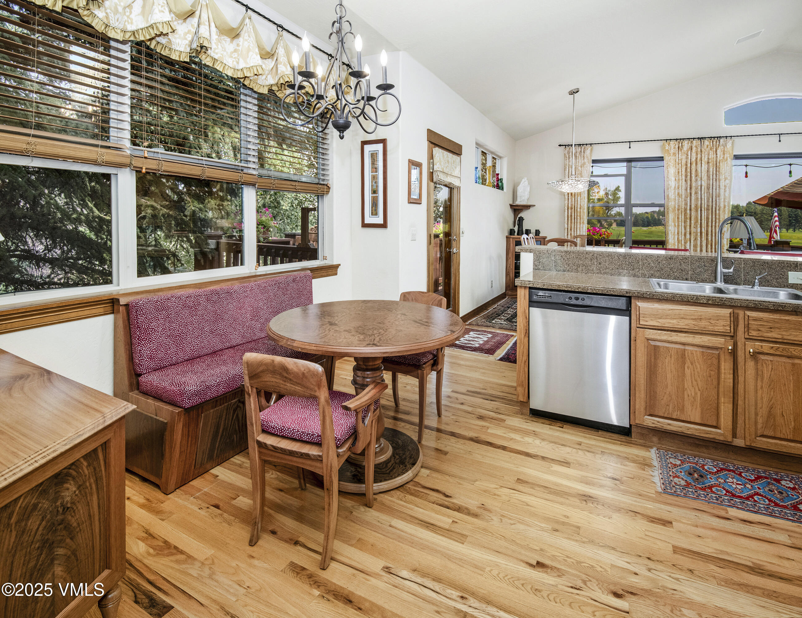 Kitchen and dining area with a red banquette, round wood table, and large windows overlooking a golf course.