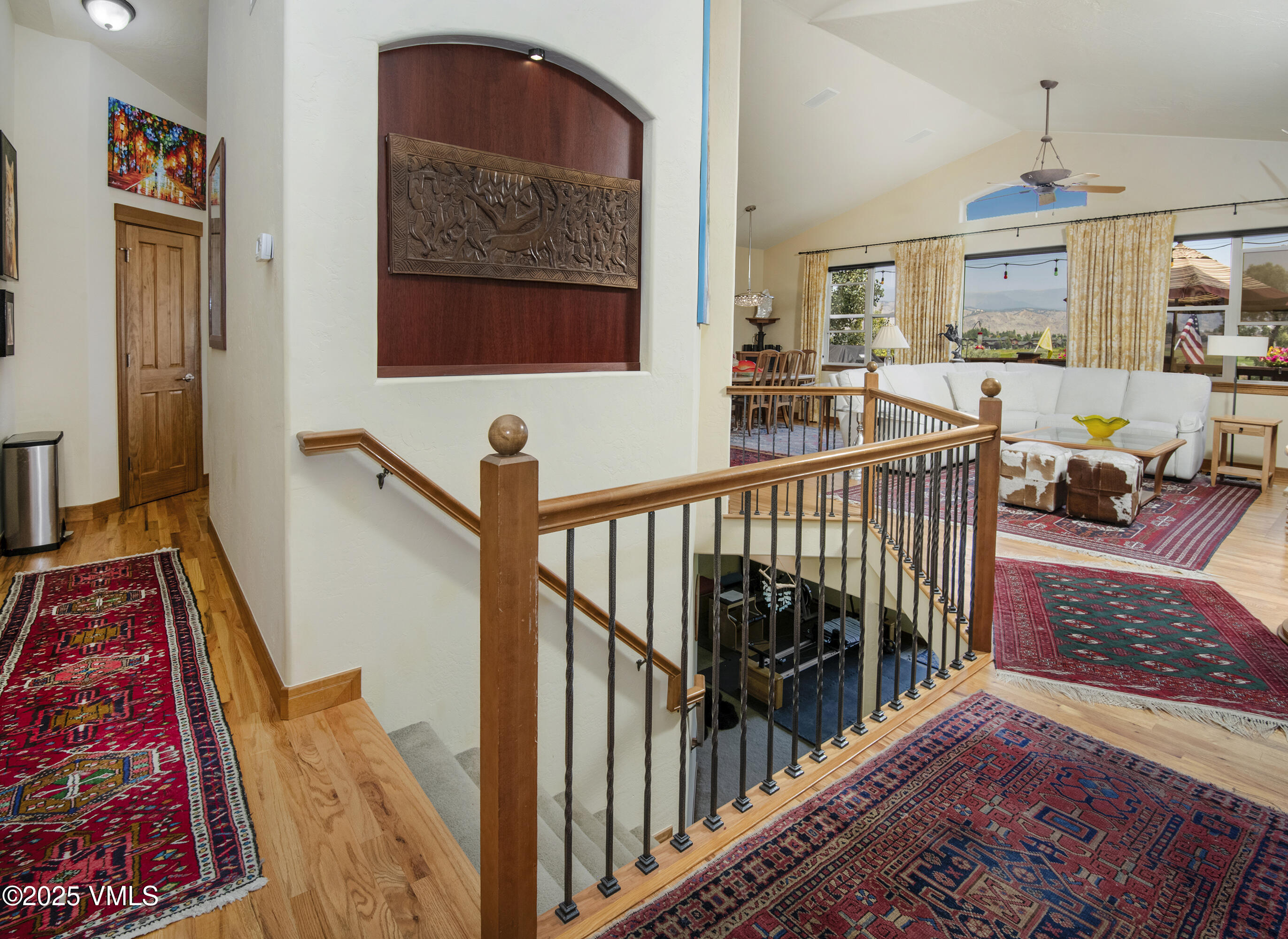 Living room with a stair railing, patterned rugs, and mountain views through large windows.