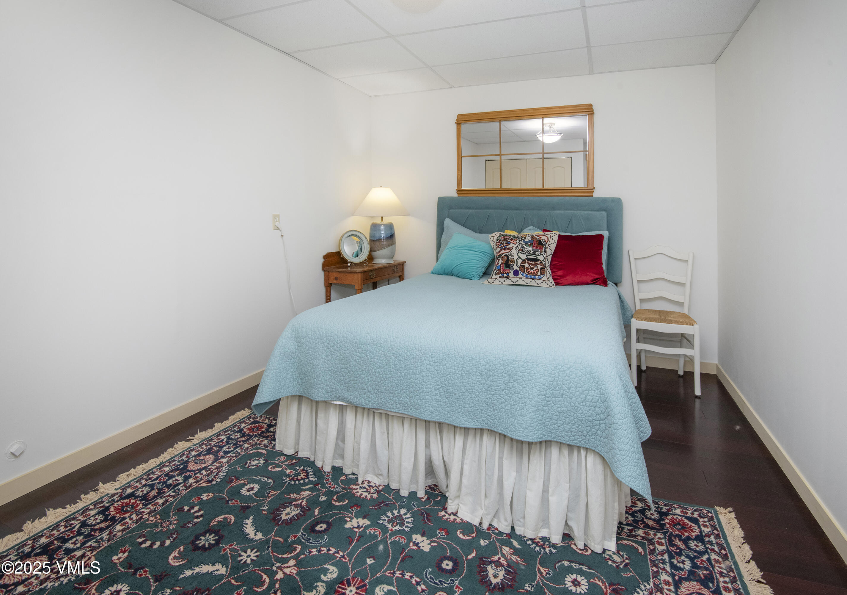 Bedroom with a light blue quilt, teal headboard, colorful pillows, and patterned rug.