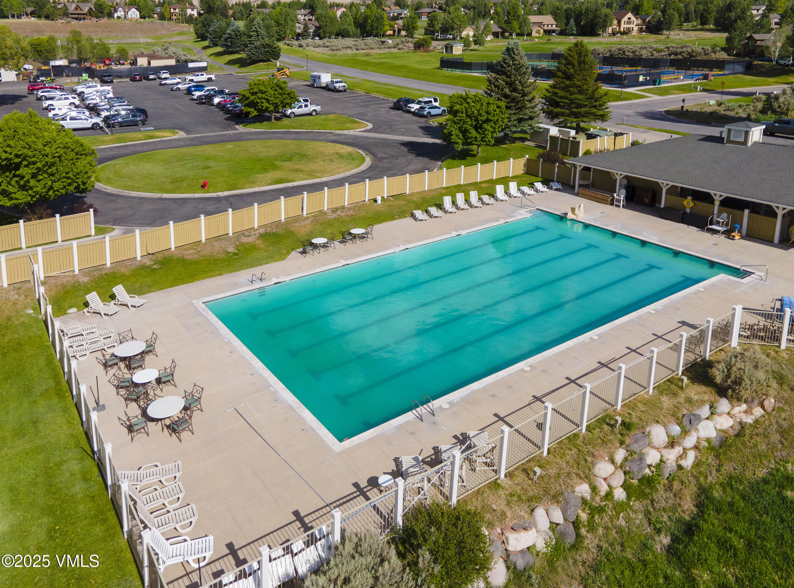 Outdoor swimming pool with a fenced deck, lounge chairs, and nearby covered pool building.