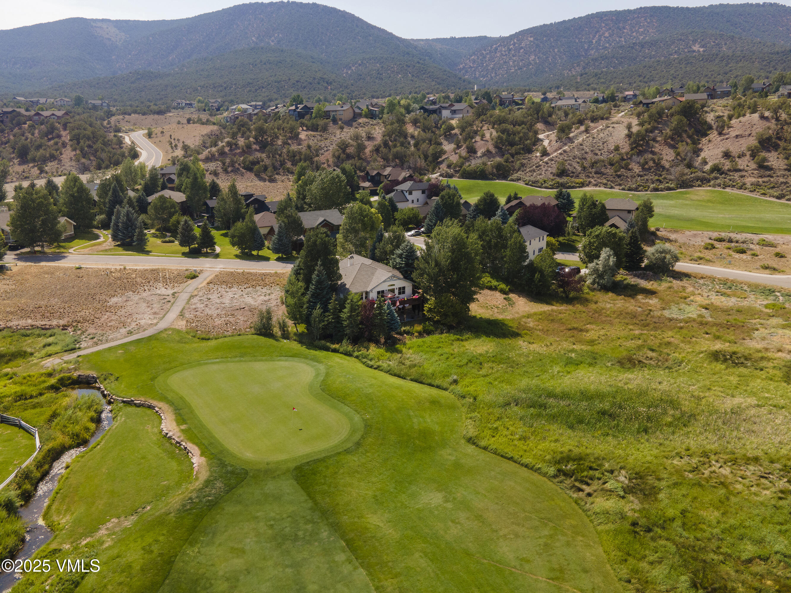 Aerial view of homes beside a golf course, with a putting green, creek, and mountain backdrop.