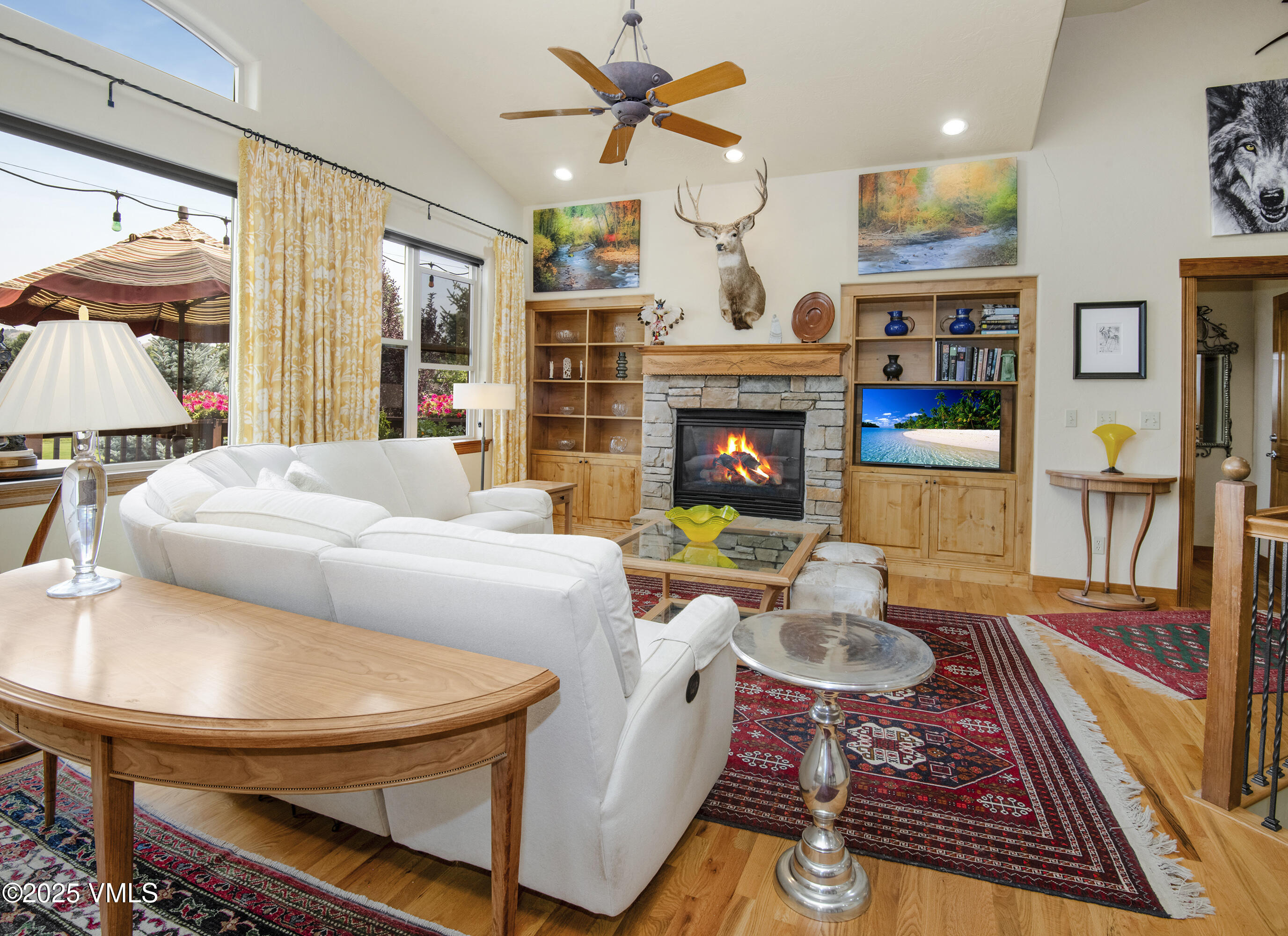 Living room with white sofas, a stone fireplace, and built-in wooden shelving.