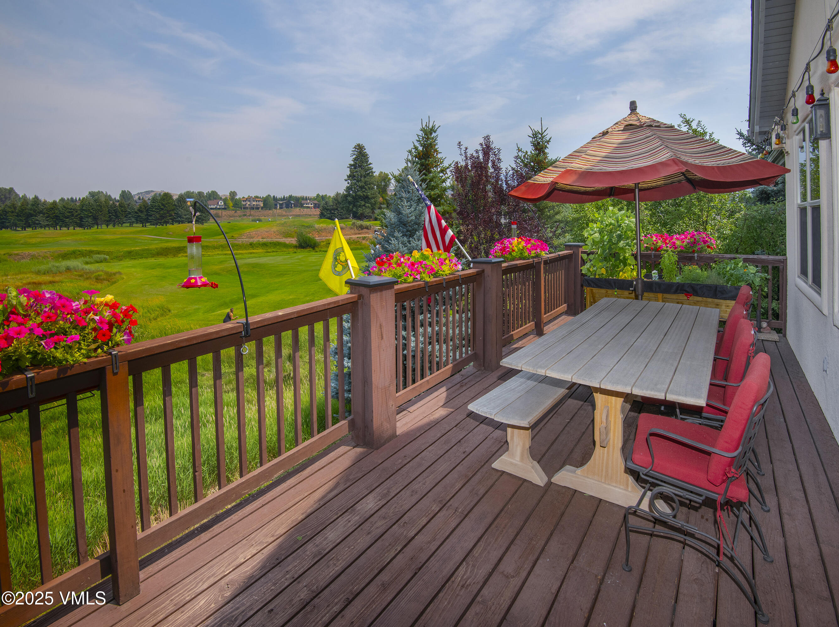 Wooden deck with outdoor dining set and striped umbrella overlooking a green golf course.