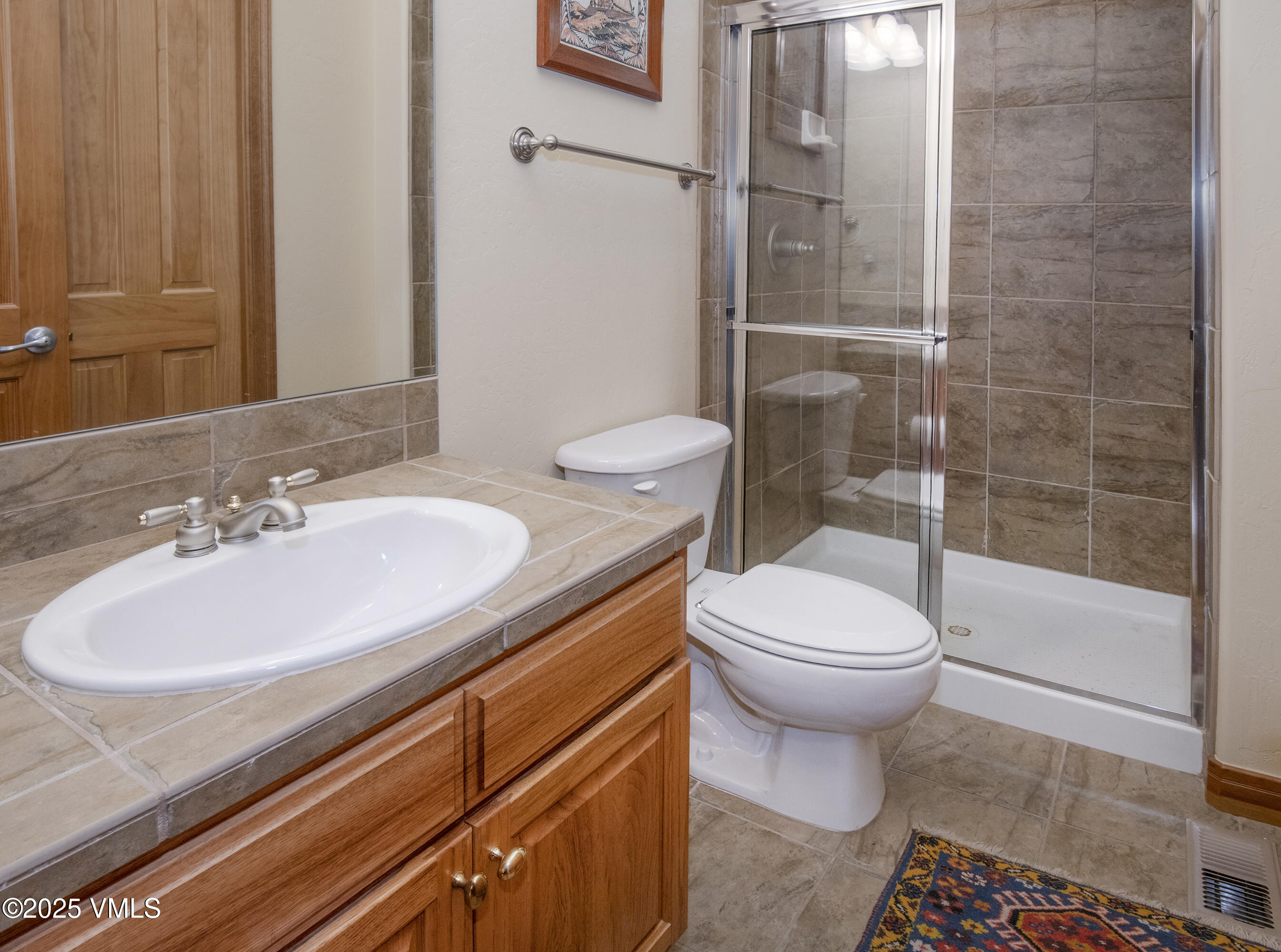 Bathroom with a tiled wood vanity, white sink, toilet, and glass-enclosed shower.