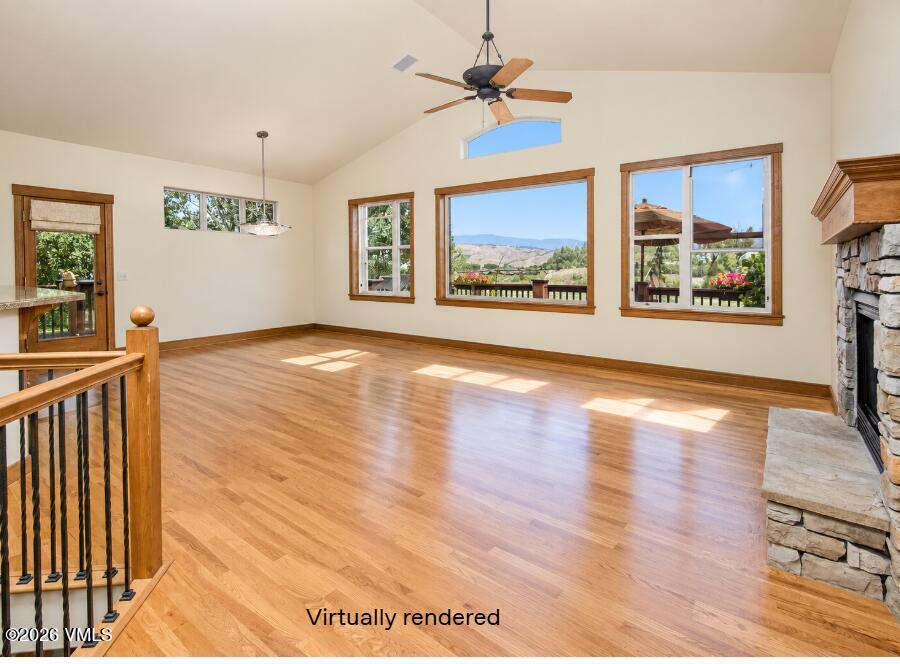 Unfurnished living room with hardwood floors, a stone fireplace, and mountain views through large windows.