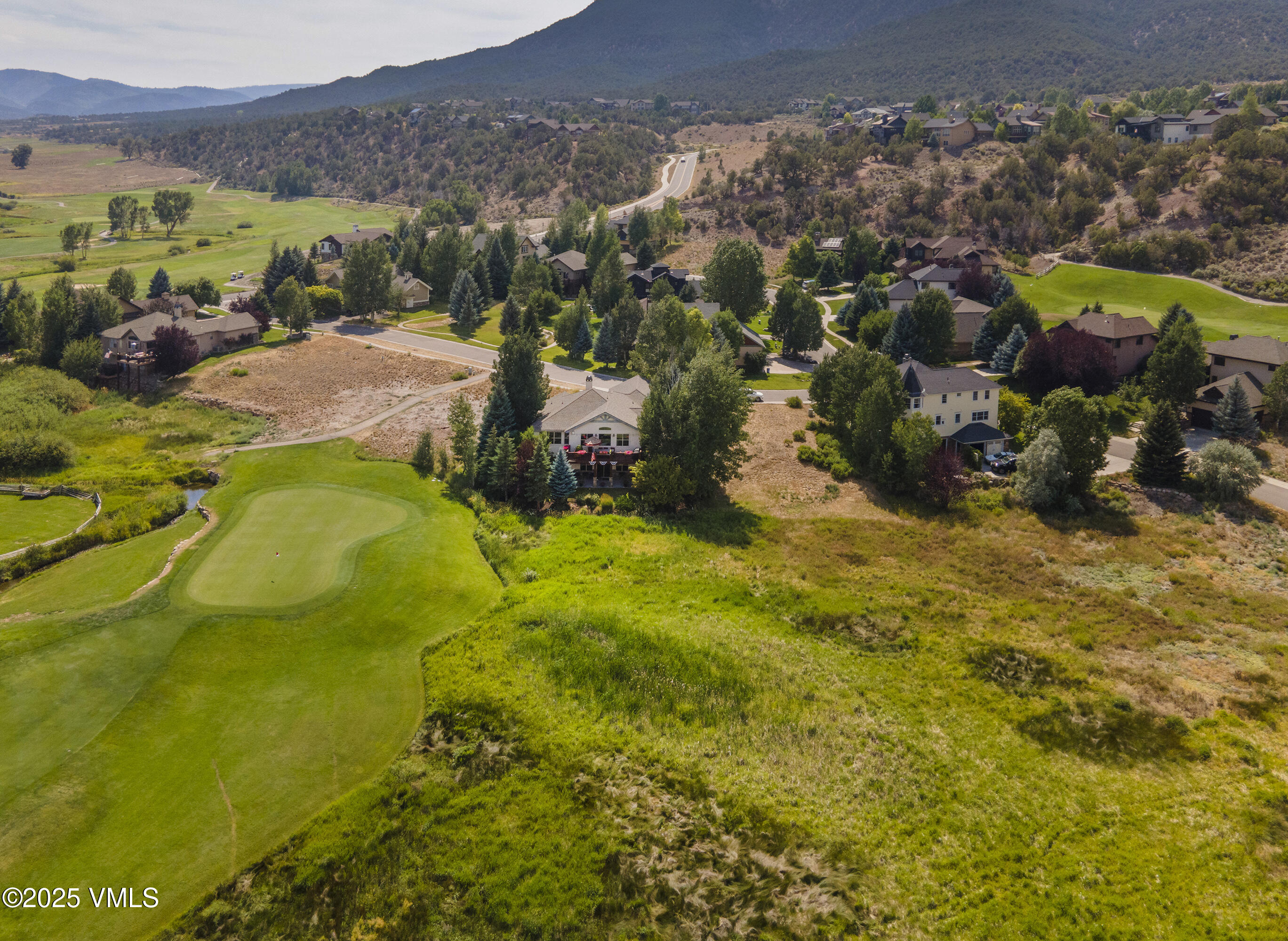 Aerial view of homes bordering a golf course, with mountains beyond.